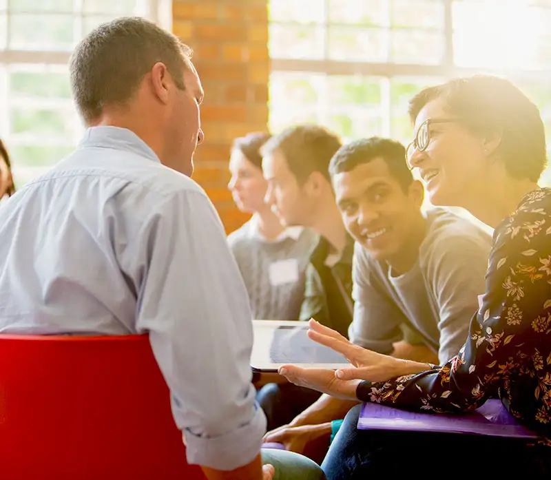 Woman with digital tablet speaking to man at group therapy session