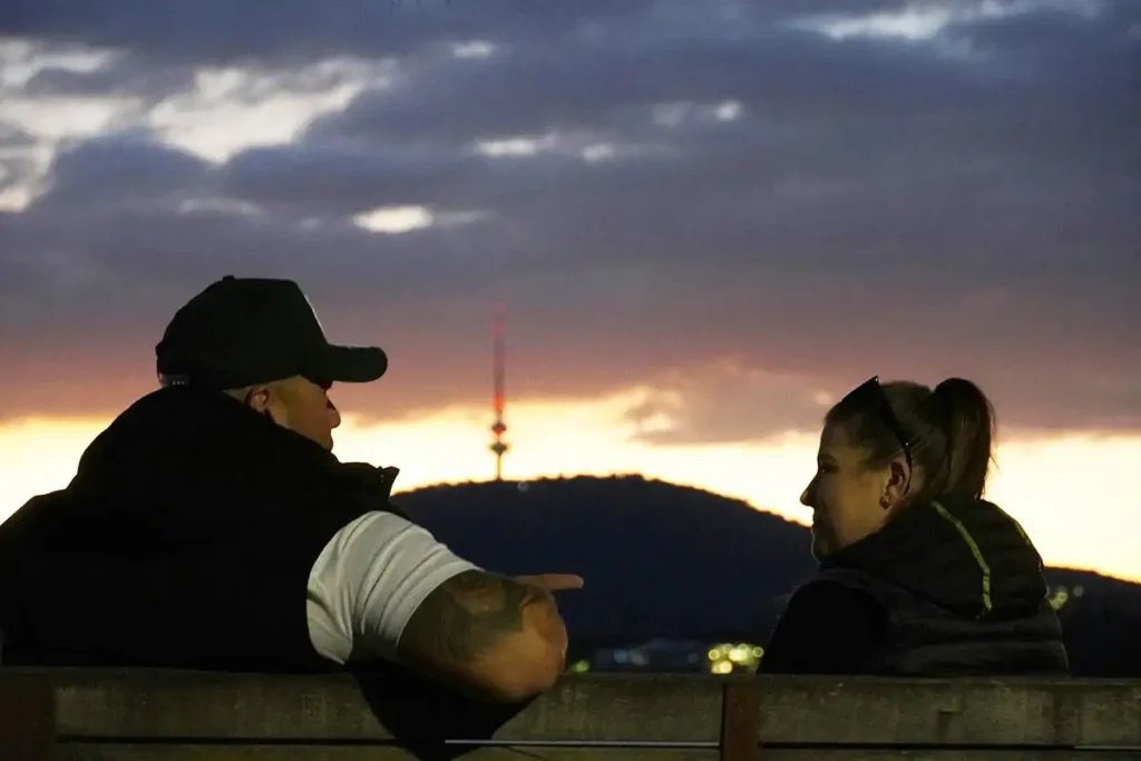 A man and woman sit on a bench at sunset, discussing about depression and alcoholism