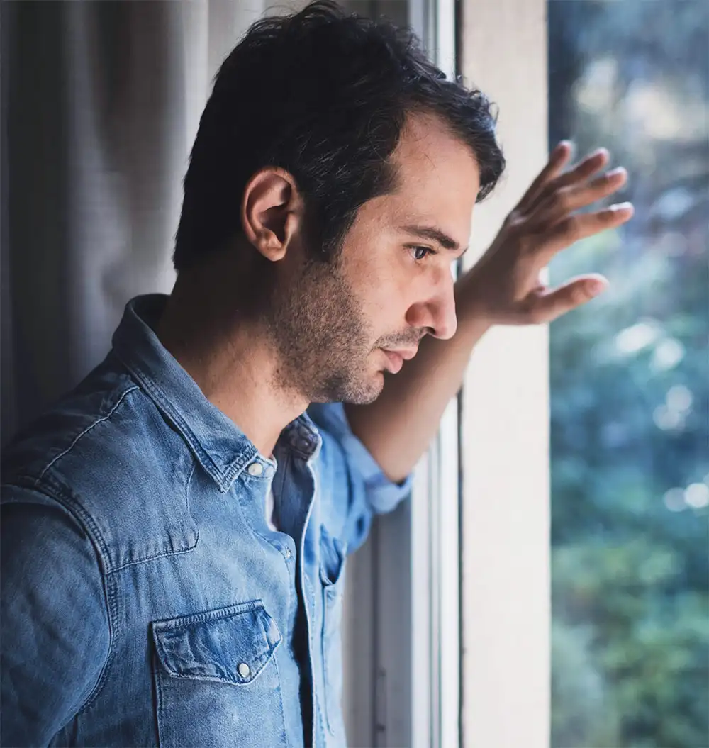 A man gazes out a window, his expression reflecting sadness and contemplation