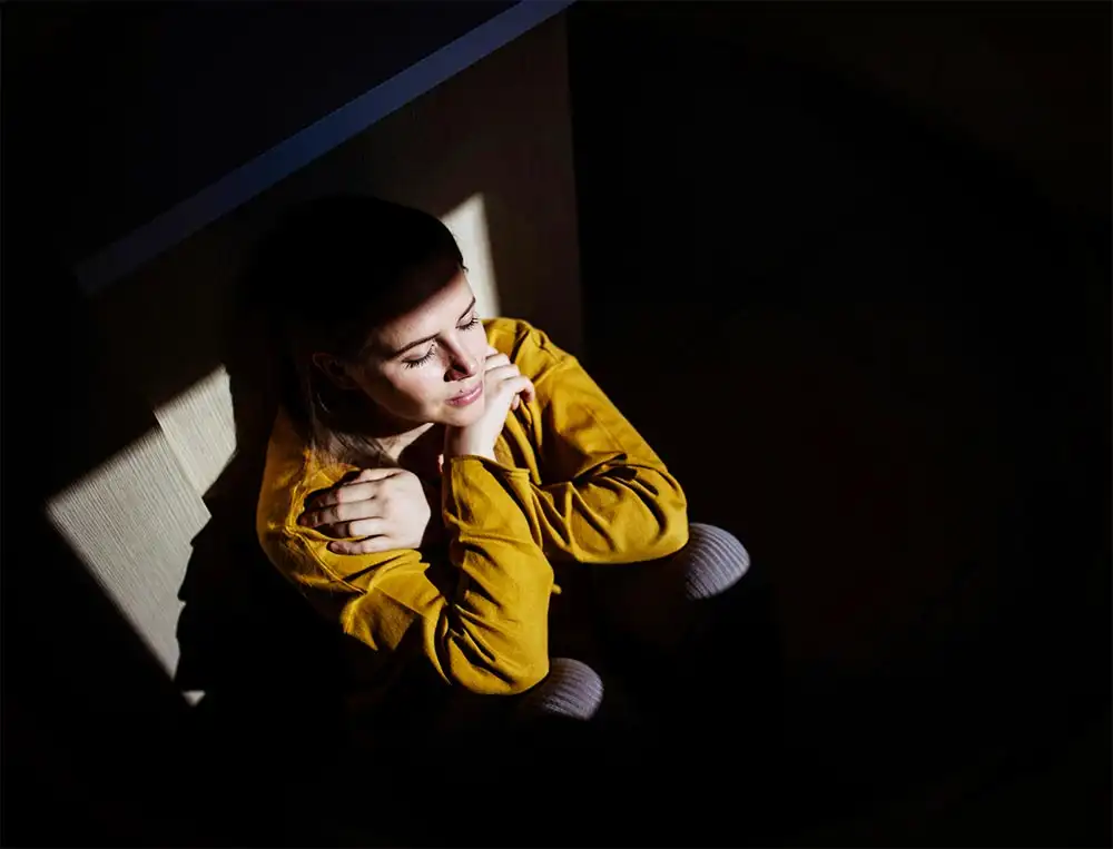 A woman sits in a dimly lit room with her arms crossed, reflecting a sense of contemplation related to Post-Traumatic Stress Disorder